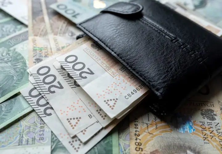 Czarny portfel na stosie polskich banknotów 100 i 200 zł.