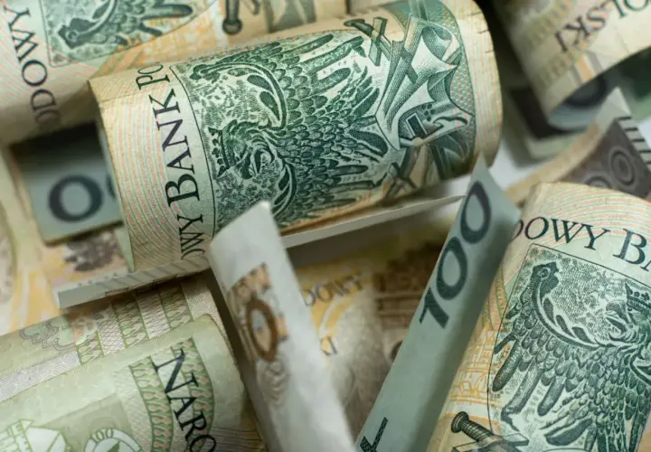 Zwijane banknoty 100 zł, czyli kosiniakowe, tworzą stos. Widoczny orzeł i napis Narodowy Bank Polski.