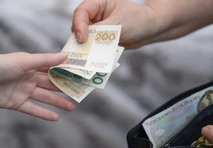 Dwie ręce przekazują sobie polskie banknoty 200 zł i 500 zł z portfela.