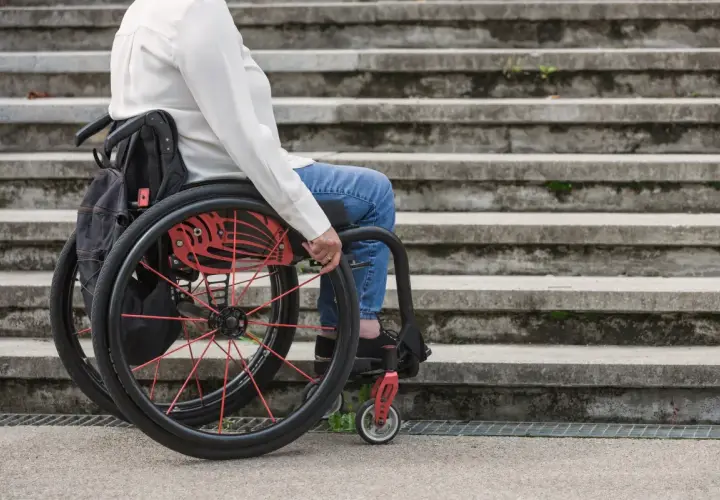 Osoba na wózku inwalidzkim, część grupy inwalidzkiej, siedzi przed kamiennymi schodami.