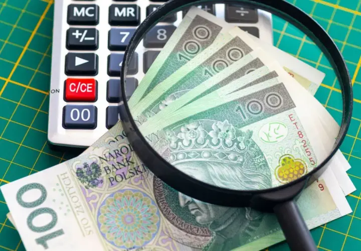 Kalkulator, szkło powiększające i banknoty 100 zł na zielonej macie.