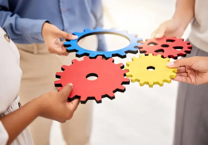 Dłonie łączą kolorowe trybiki, symbolizując współpracę i mechanizm.