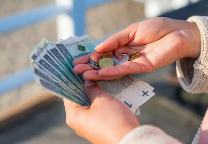 Dłonie trzymające polskie banknoty i monety.