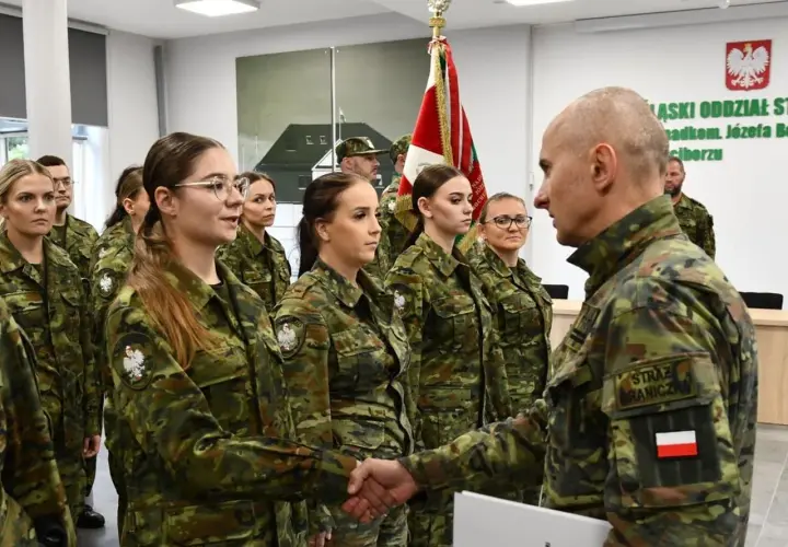 Uroczystość w Straży Granicznej: funkcjonariuszka ściska dłoń przełożonemu, w tle inni funkcjonariusze.