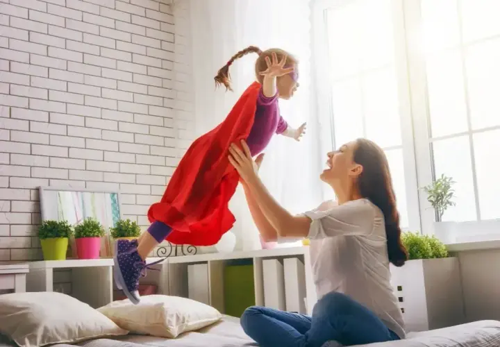 Radosna dziewczynka w stroju superbohaterki lata w górę, złapana przez uśmiechniętą mamę. To wspaniałe, babciowe chwile pełne zabawy.