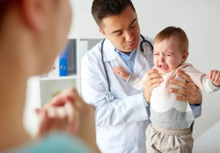 Lekarz uspokaja płaczące dziecko, które przechodzi trudny skok rozwojowy. Mama patrzy z troską.