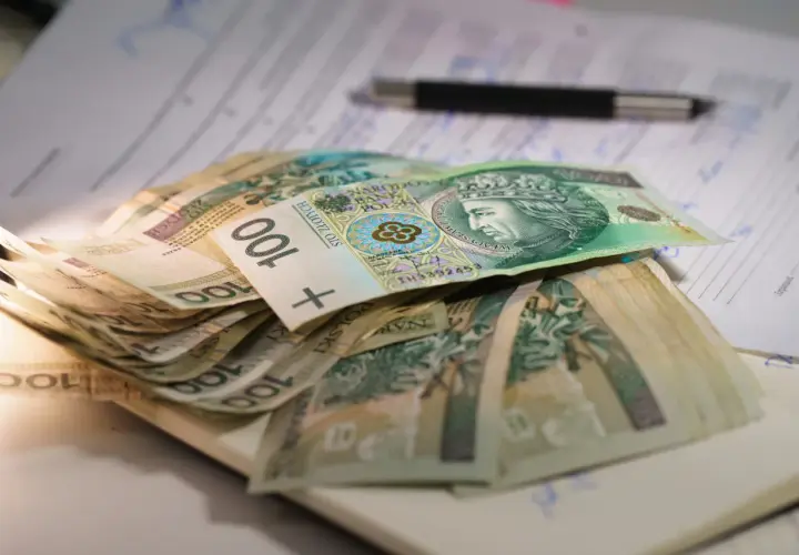 Stos banknotów 100 zł leży na dokumentach. Może to być związane z oceną stopnie niepełnosprawności i przyznawanymi świadczeniami.