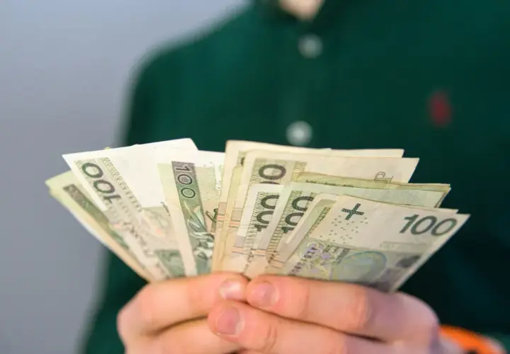 Dłonie trzymają wachlarz banknotów 100 zł. Może to być wypłata, oszczędności lub emerytura.