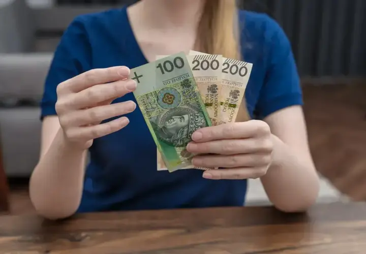 Dłonie trzymające polskie banknoty: 100 zł i dwa razy po 200 zł.