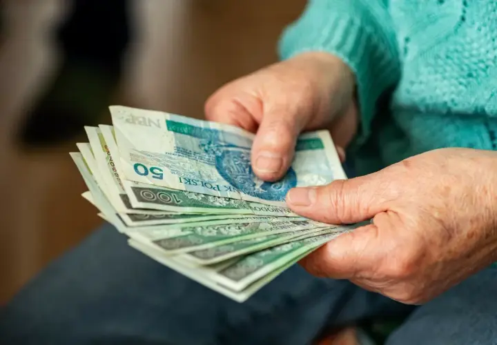 Dłonie starszej osoby trzymające stos polskich banknotów.