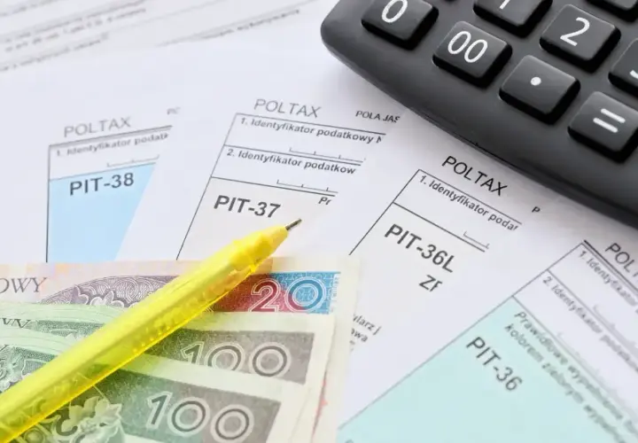 Formularze PIT, polskie banknoty, żółty długopis i kalkulator.