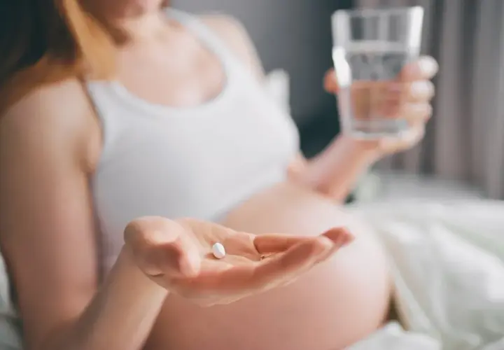 Kobieta w ciąży bierze tabletkę i popija ją wodą, dbając o prawidłowe ciśnienie w ciąży.