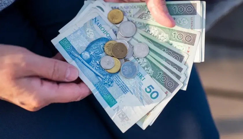 Dłonie trzymają polskie banknoty i monety. Czy mam 60 lat i 10 lat pracy, czy dostanę emeryturę?