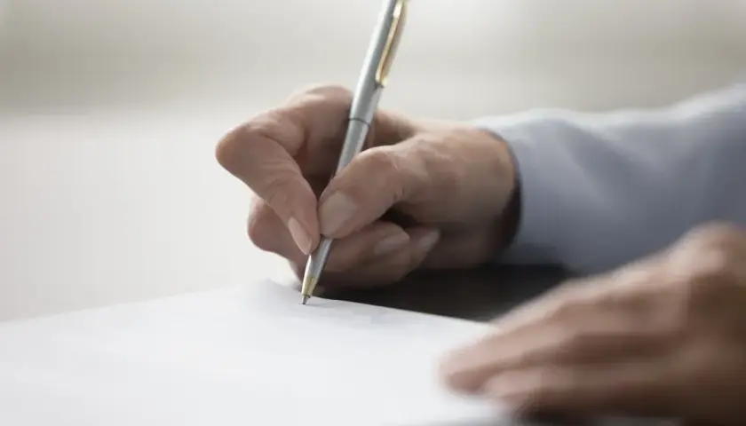 Dłoń pisząca długopisem po białej kartce papieru.
