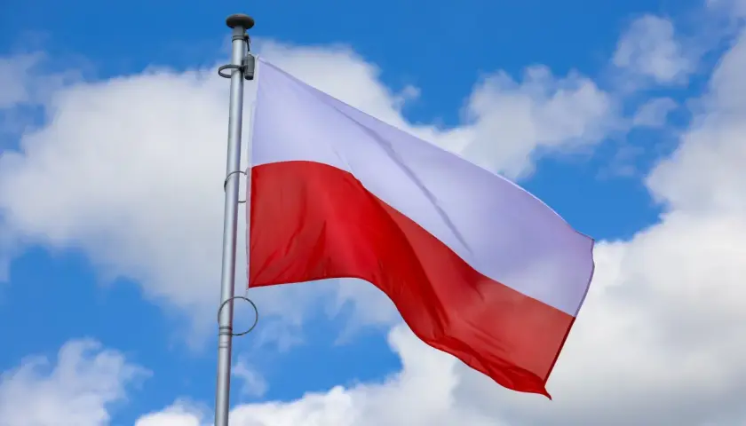 Biało-czerwona flaga Polski powiewa na tle błękitnego nieba z chmurami. Czy 2 maja jest wolny? To pytanie zadają sobie Polacy, ciesząc się świętem narodowym.