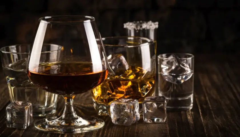 Kilka szklanek z różnymi alkoholami i lodem na drewnianym stole.
