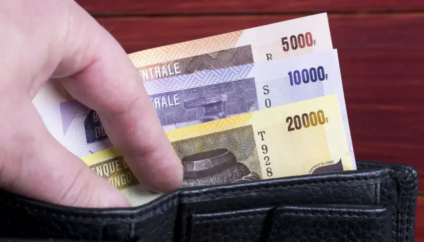 Dłoń wsuwa banknoty o nominałach 5000, 10000 i 20000 do czarnego portfela.