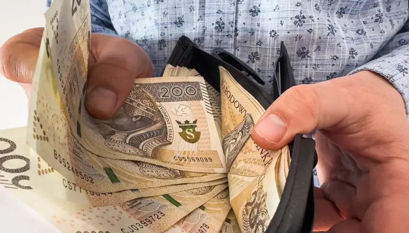 Dłonie trzymające portfel z polskimi banknotami 200 zł.