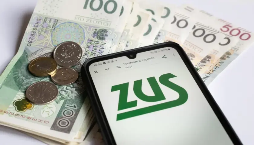 Polskie banknoty i monety obok smartfona z logo ZUS.