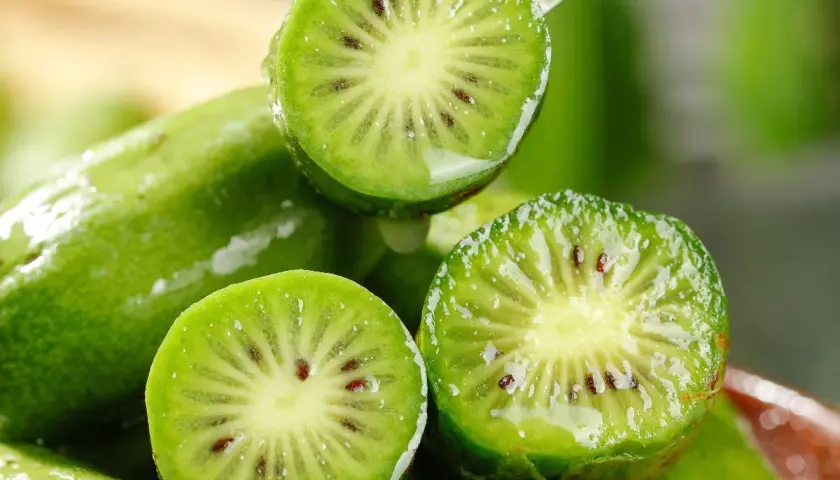 Przekrojone na pół, mokre kiwi z widocznymi pestkami na tle innych owoców.