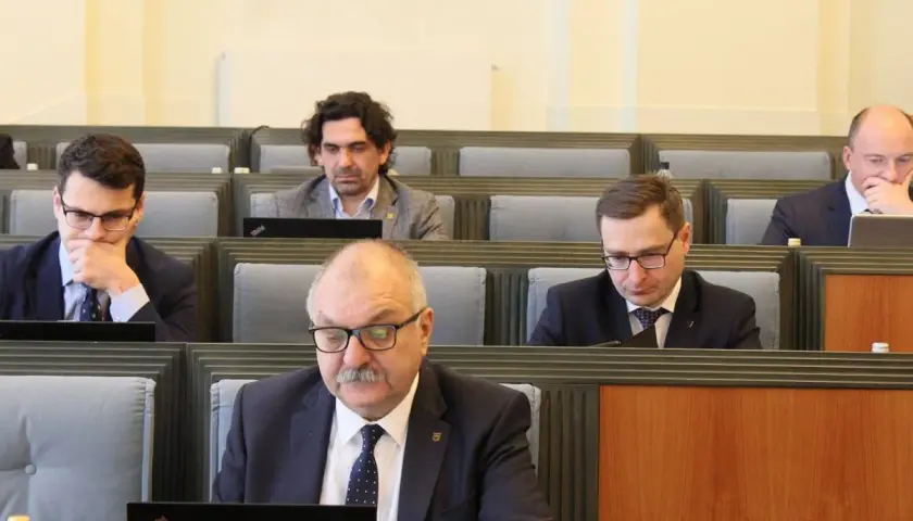 Mężczyźni w garniturach siedzą w rzędach, patrząc na laptopy.