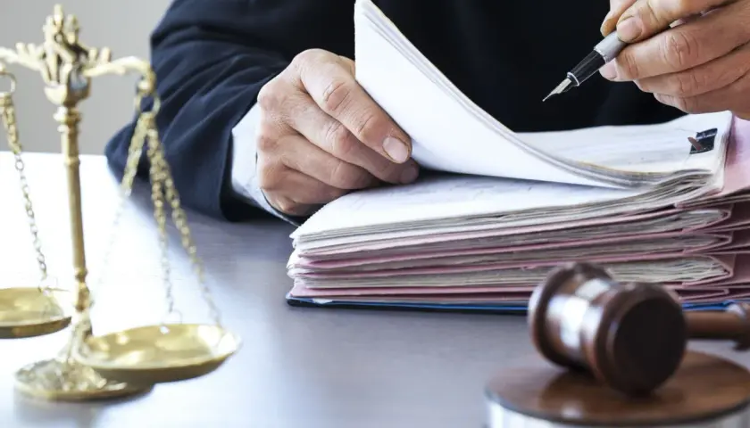 Sędzia w todze przegląda dokumenty, obok waga sprawiedliwości i młotek.