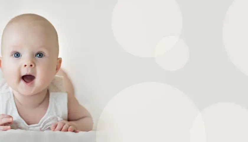 Uśmiechnięte niemowlę z otwartymi ustami leży na brzuchu na jasnym tle z okręgami.