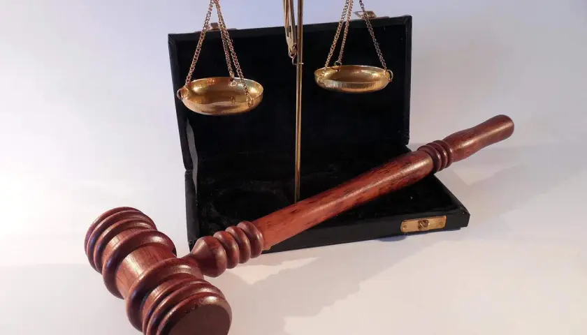 Młotek sędziowski i waga szalkowa na tle otwartego czarnego etui.