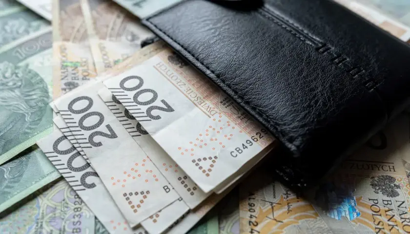 Czarny portfel na stosie polskich banknotów 100 i 200 zł.