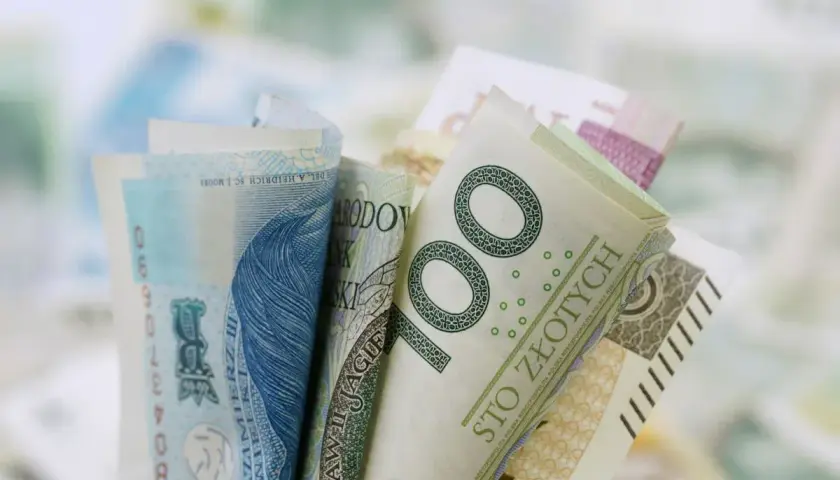 Zwoje polskich banknotów, w tym 100 złotych, na rozmytym tle.