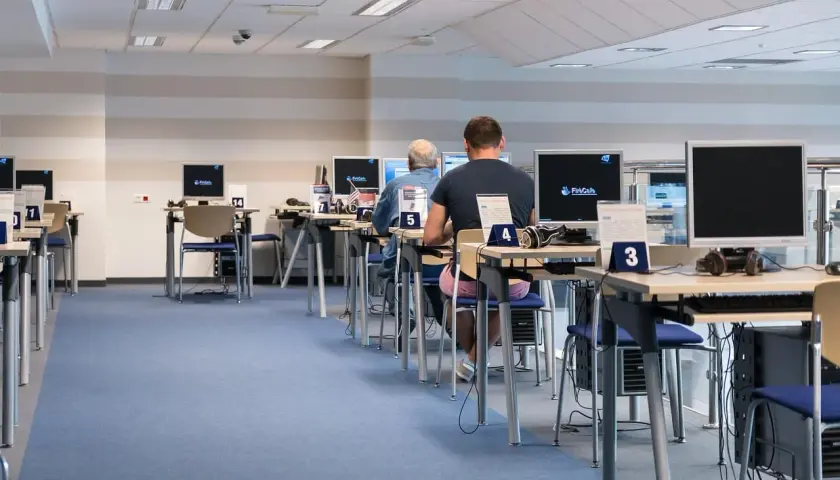 Rząd stanowisk komputerowych z osobami pracującymi, niebieska wykładzina.