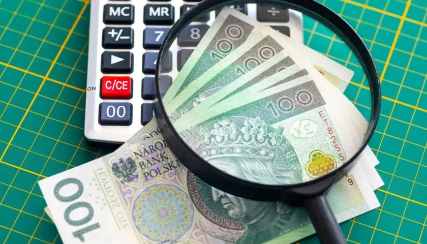 Kalkulator, szkło powiększające i banknoty 100 zł na zielonej macie.
