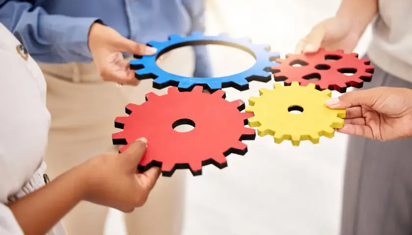 Dłonie łączą kolorowe trybiki, symbolizując współpracę i mechanizm.