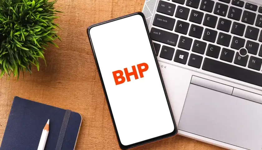 Telefon z napisem BHP na ekranie, obok laptopa, notatnika i rośliny.