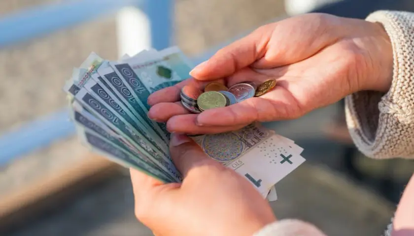 Dłonie trzymające polskie banknoty i monety.