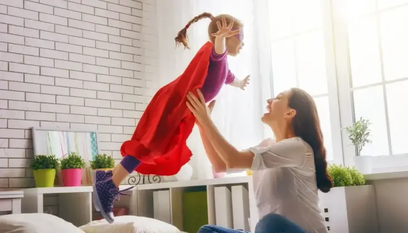 Radosna dziewczynka w stroju superbohaterki lata w górę, złapana przez uśmiechniętą mamę. To wspaniałe, babciowe chwile pełne zabawy.