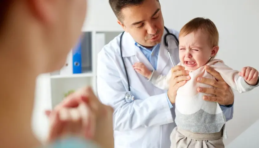 Lekarz uspokaja płaczące dziecko, które przechodzi trudny skok rozwojowy. Mama patrzy z troską.