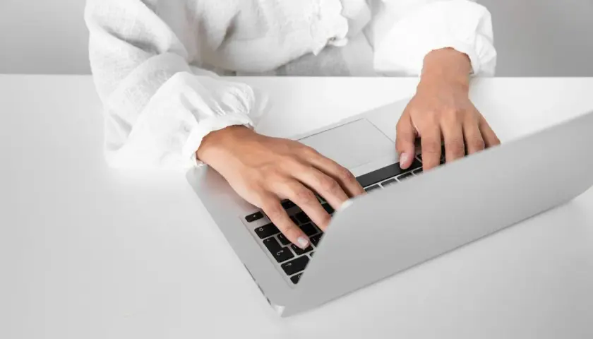 Dłonie piszące na klawiaturze laptopa na białym biurku.