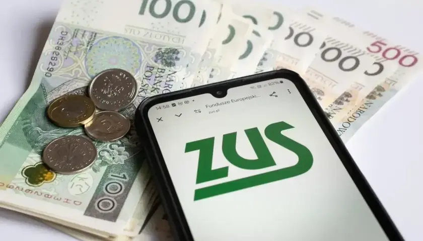 Telefon z logo ZUS na ekranie, obok polskie banknoty i monety.