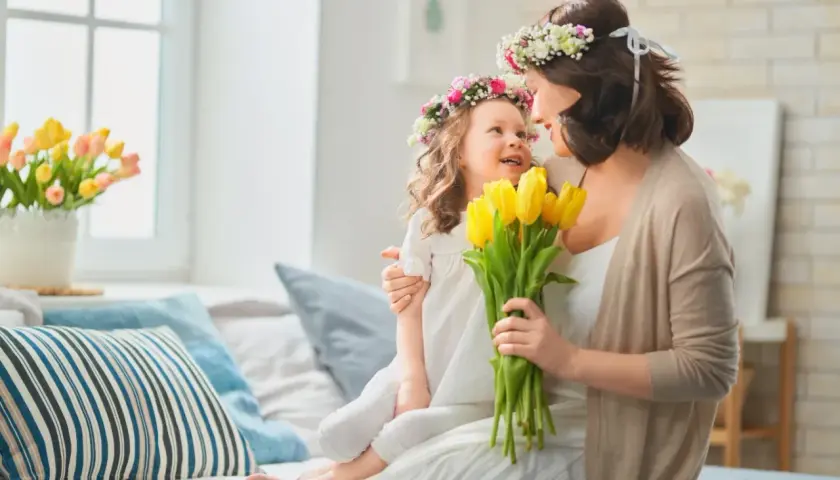 Matka i córka w wiankach z kwiatów, trzymają bukiet żółtych tulipanów.