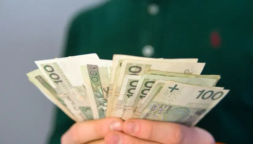 Dłonie trzymają wachlarz banknotów 100 zł. Może to być wypłata, oszczędności lub emerytura.