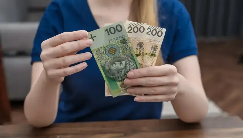 Dłonie trzymające polskie banknoty: 100 zł i dwa razy po 200 zł.