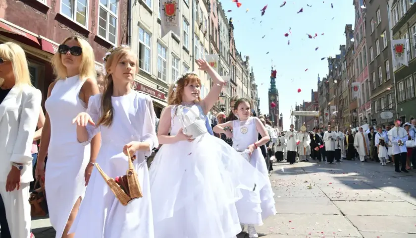 Procesja Bożego Ciała na ulicy, dzieci w białych strojach sypią płatki róż.