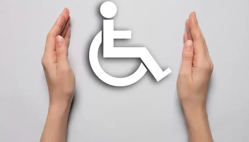 Dwie dłonie otaczają biały symbol osoby na wózku inwalidzkim na jasnoszarym tle.
