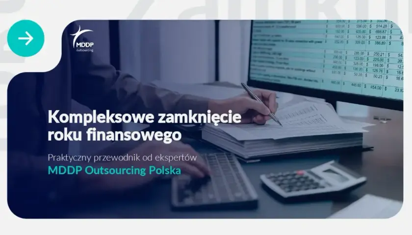 Osoba pisząca ręcznie na dokumentach przy biurku z komputerem i kalkulatorem.