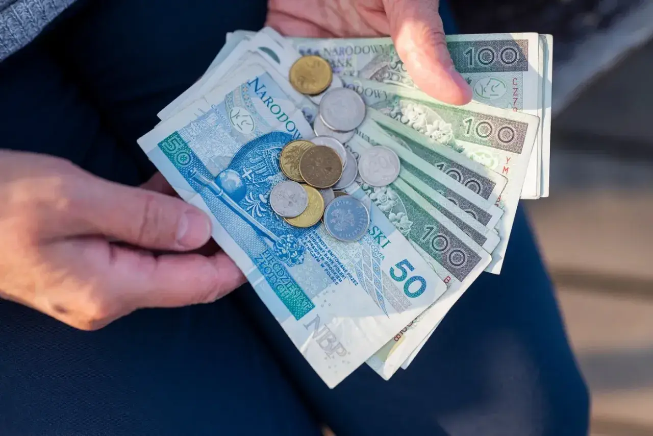 Dłonie trzymają polskie banknoty i monety. Czy mam 60 lat i 10 lat pracy, czy dostanę emeryturę?