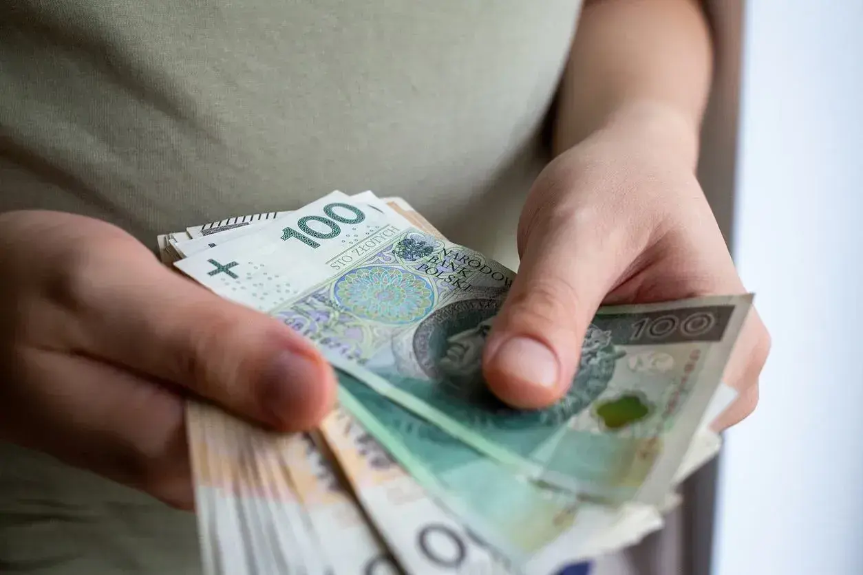 Dłonie trzymające stos banknotów 100 zł.