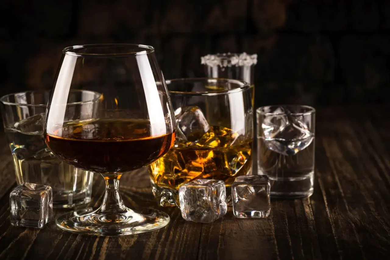 Kilka szklanek z różnymi alkoholami i lodem na drewnianym stole.