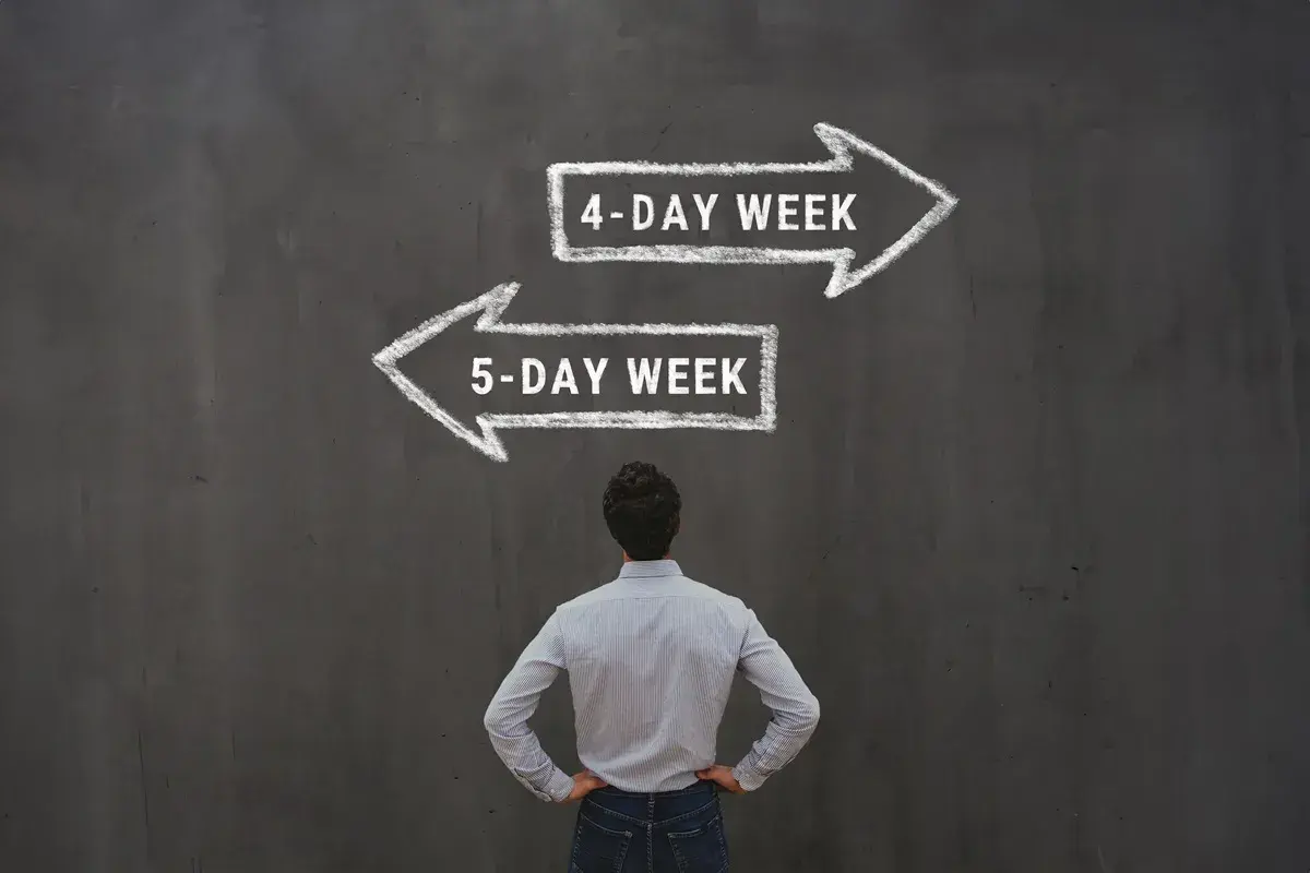 Mężczyzna stoi przed tablicą z dwoma strzałkami: "4-DAY WEEK" i "5-DAY WEEK".