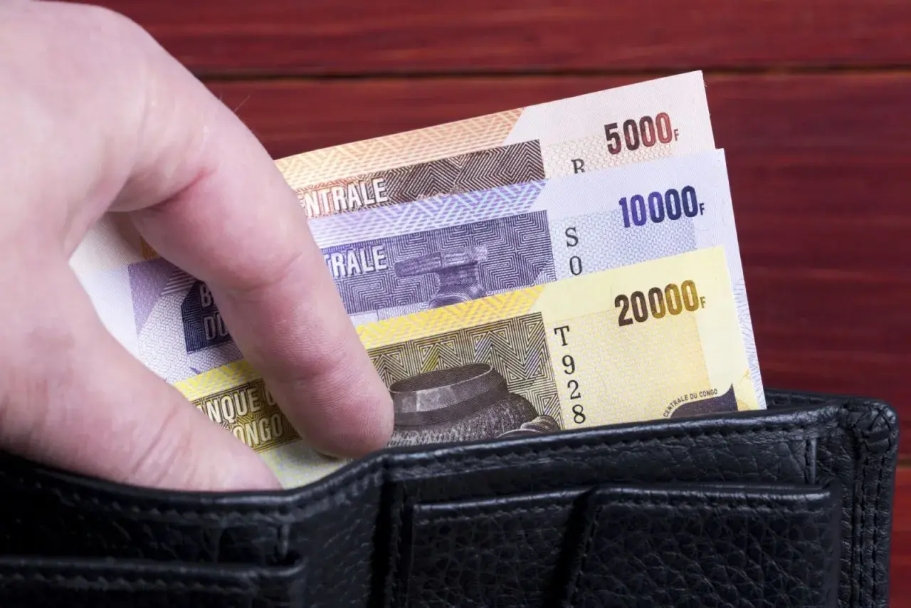 Dłoń wsuwa banknoty o nominałach 5000, 10000 i 20000 do czarnego portfela.